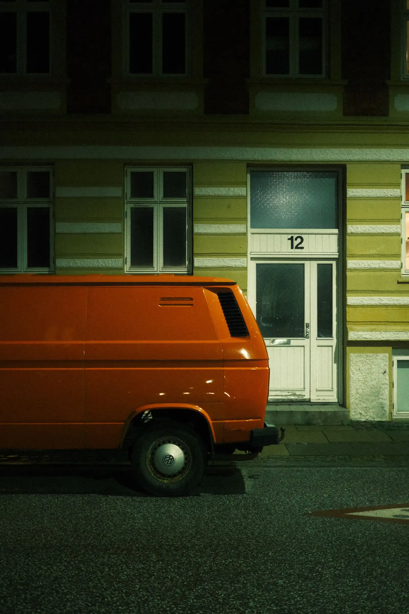 A tradesperson's van parked on a dark residential street at night, one doorway lit