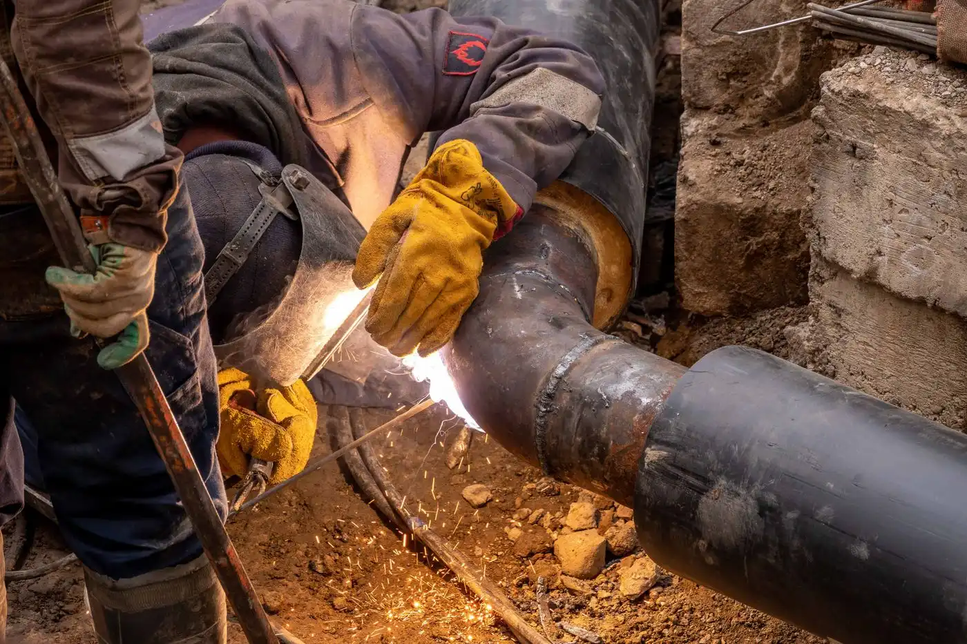 A worker welding steel pipes, sparks flying in a dark industrial space