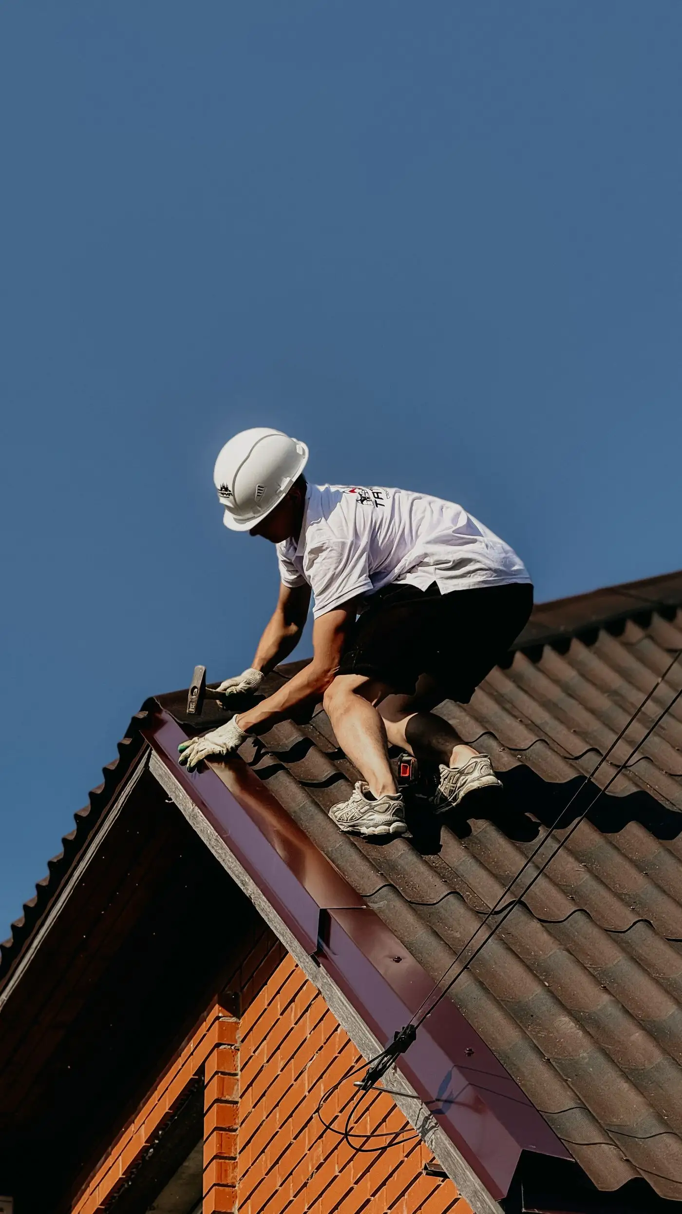 A roofer in a safety helmet renovating a brick house roof