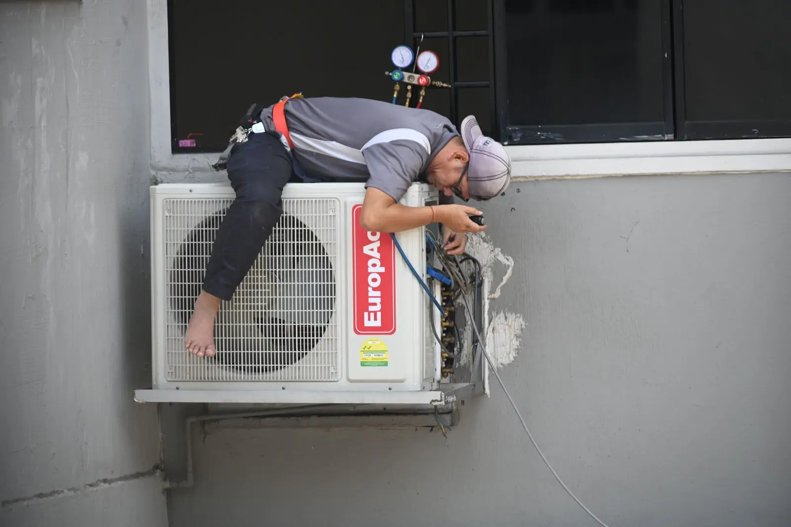 A technician repairing an outdoor air conditioning unit mounted on a building wall