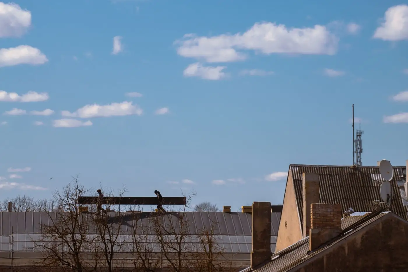 Roofers silhouetted against the sky while working on a house roof