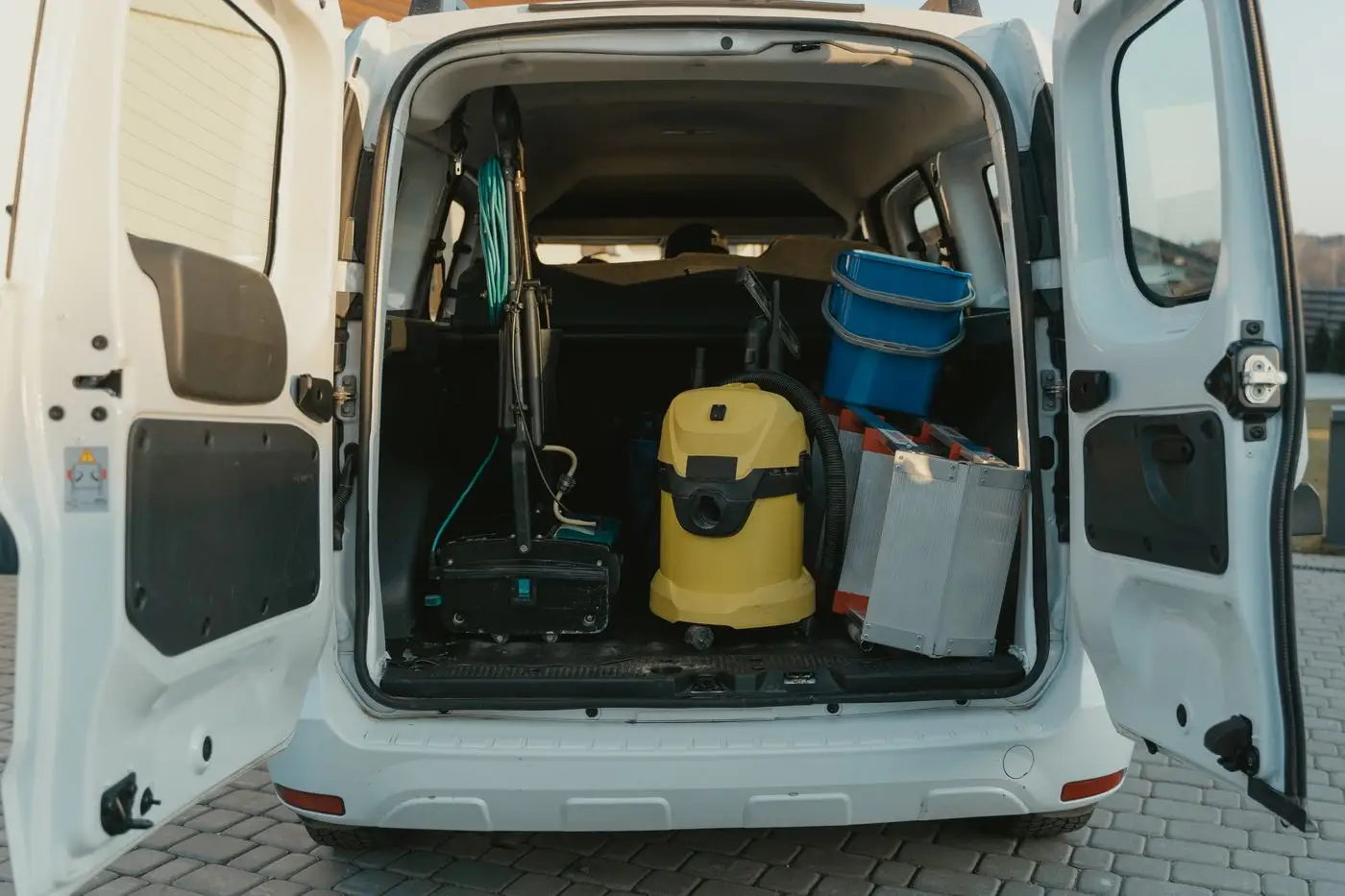 The open trunk of a cleaning service van stocked with equipment