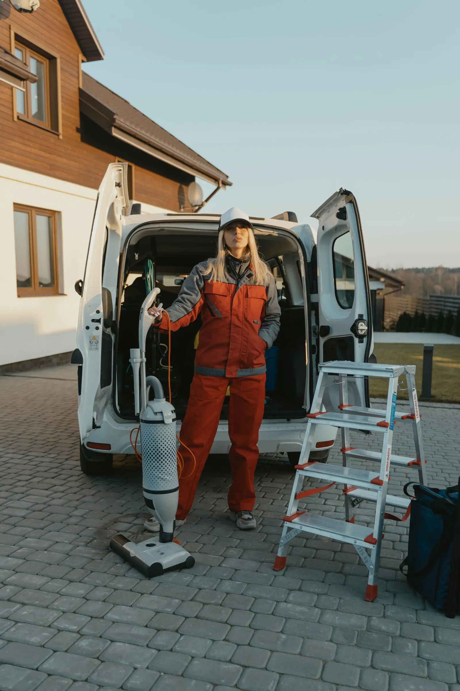 A uniformed cleaner with equipment beside her van outside a customer's house
