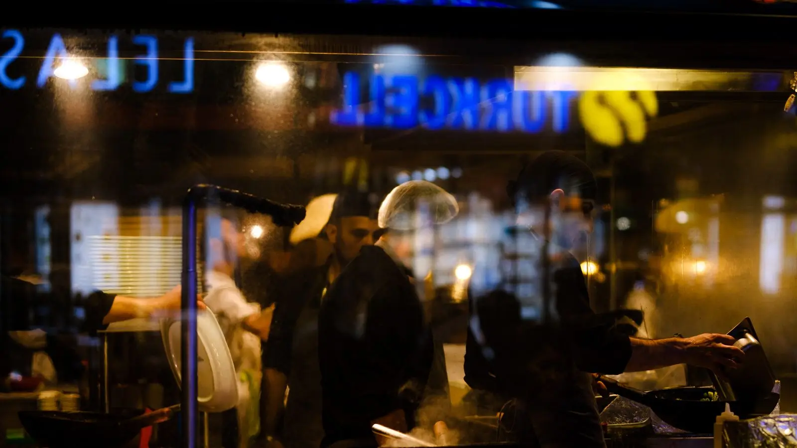 Chefs working in a restaurant kitchen at night, seen through the window